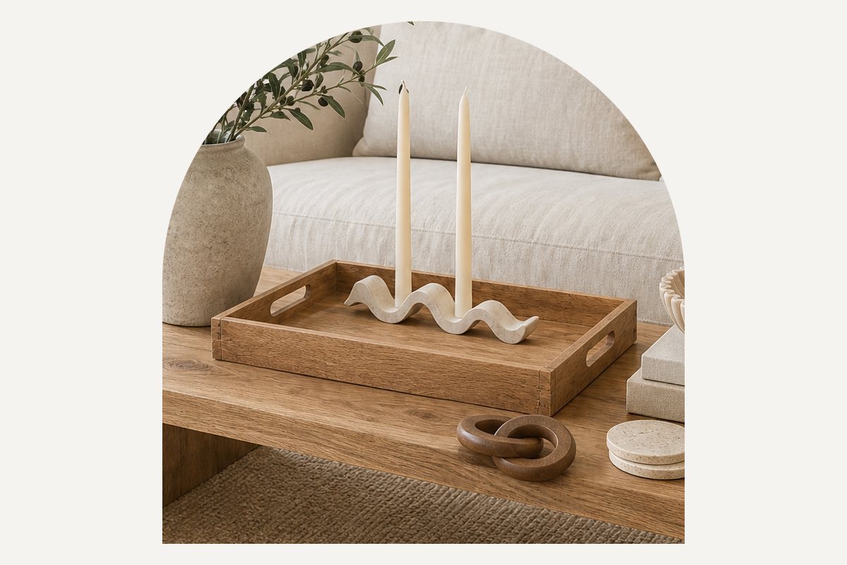 Close-up of the acacia wood tray on the oak coffee table, holding a white wave candle holder with two ivory tapers, with a wood chain link and travertine coasters beside it