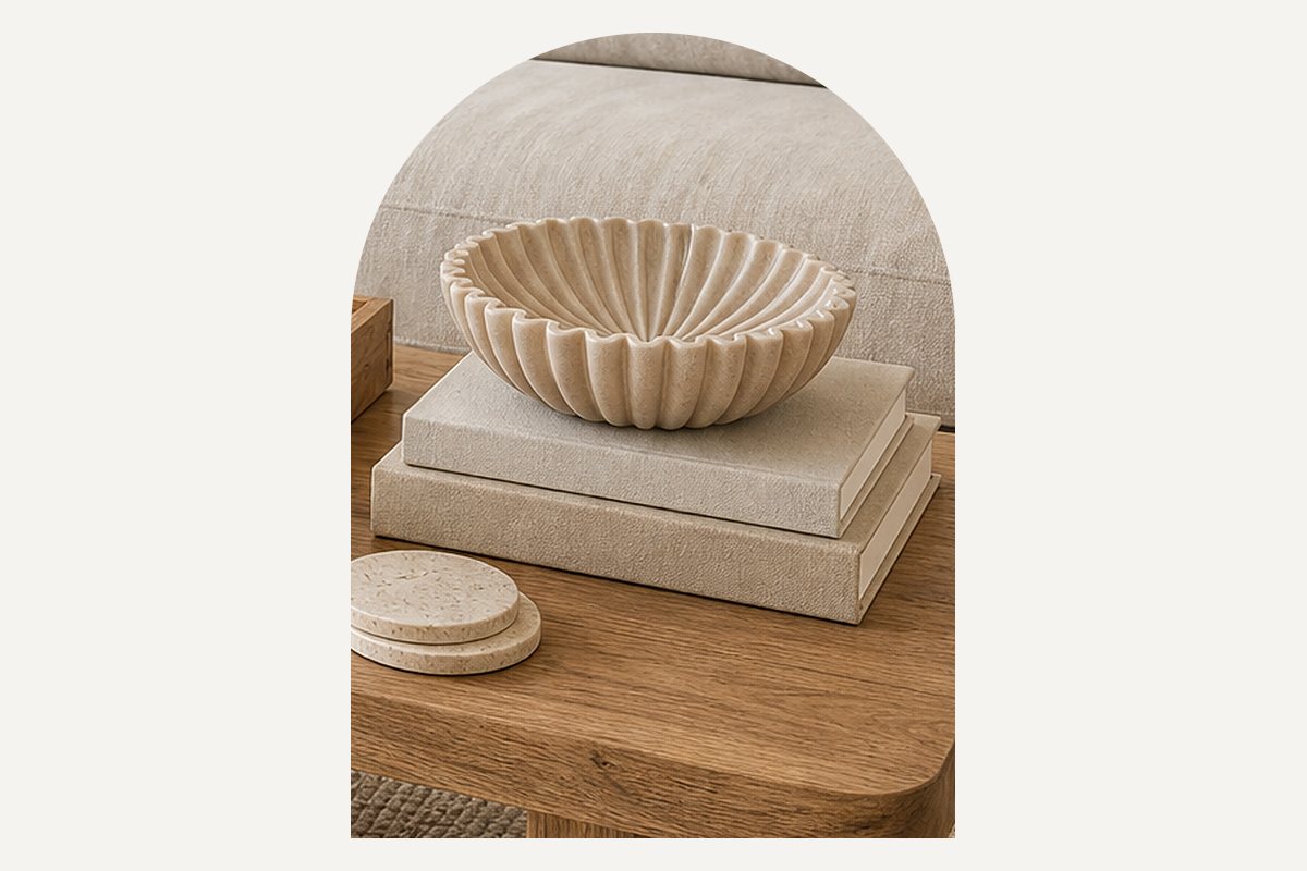 Close-up of two linen-covered hardcover books stacked on the coffee table with an empty fluted bowl on top and travertine coasters beside them