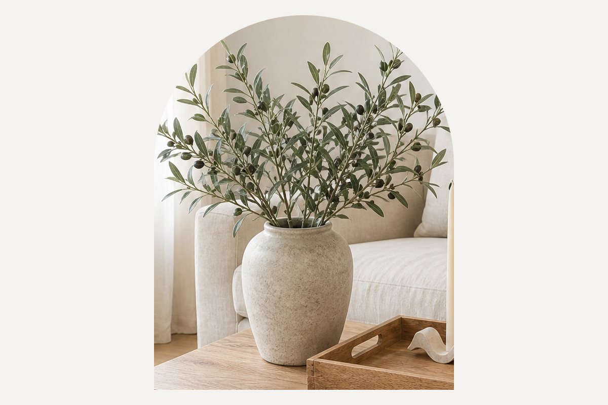 Close-up of a rustic cream ceramic vase with loose faux olive branches at one end of the coffee table